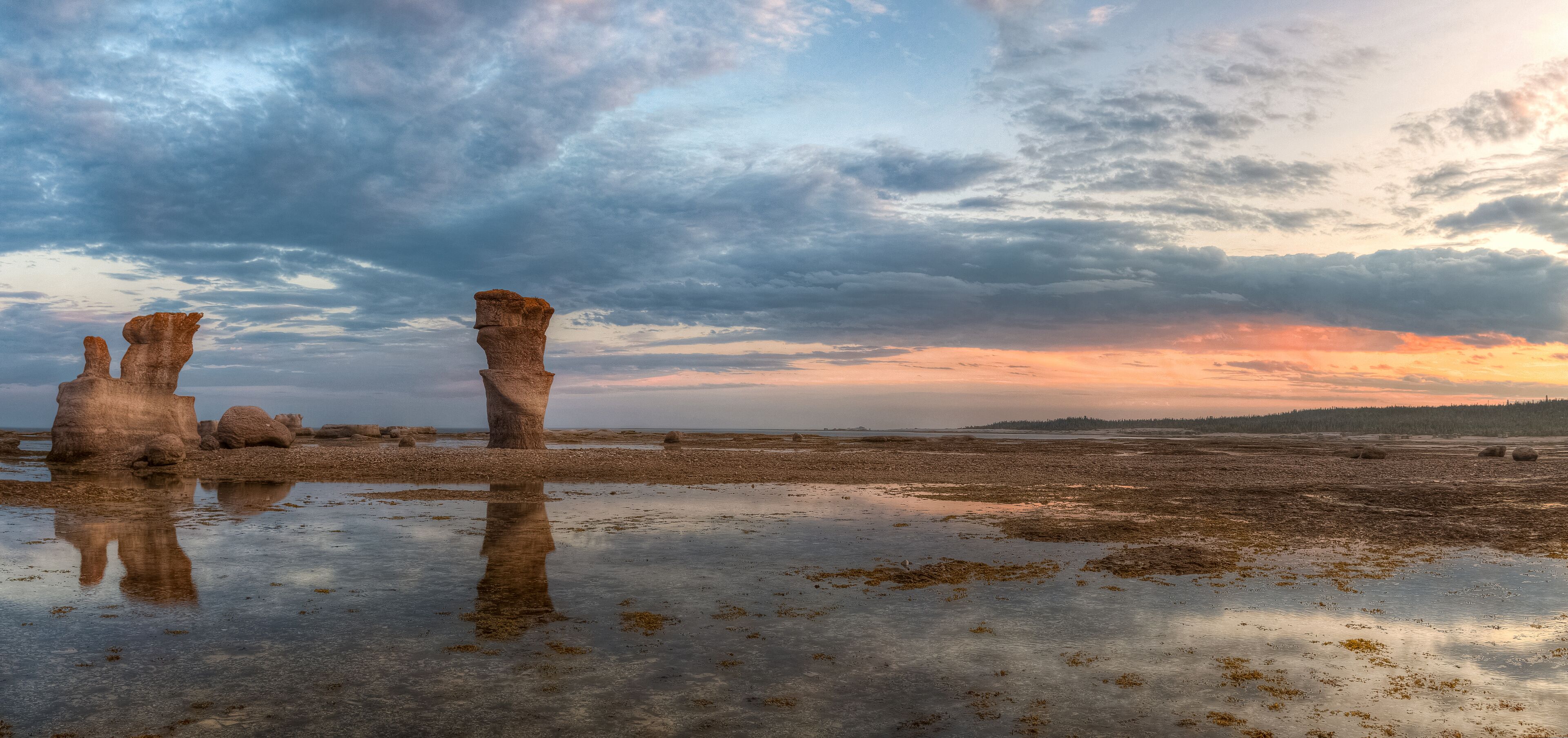 A coastal landscape with rock formations and a sunset.