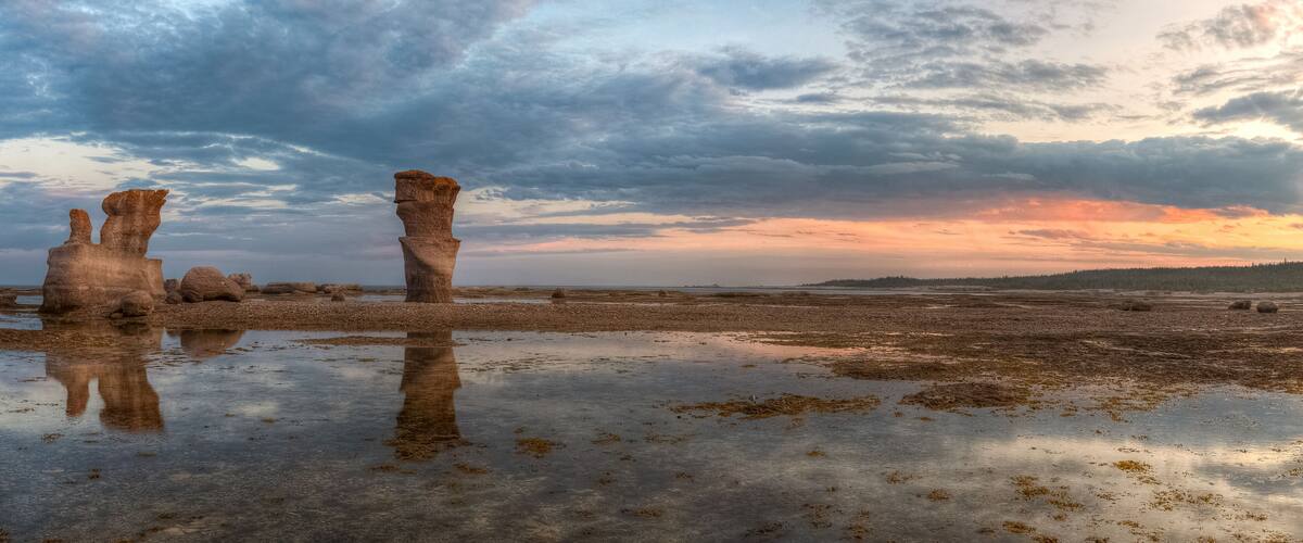 A coastal landscape with rock formations and a sunset.