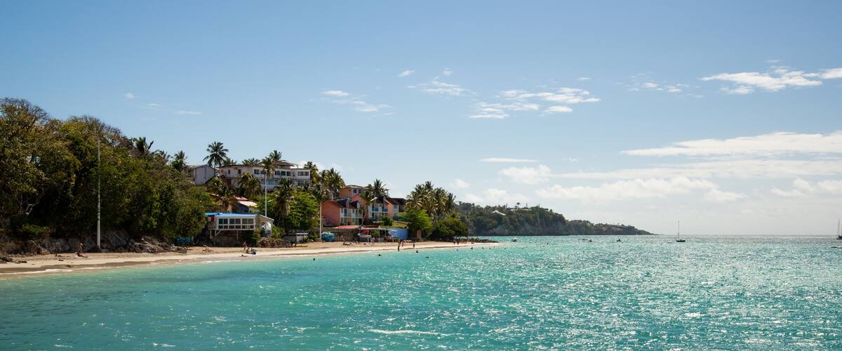 A turquoise beach with buildings and palm trees.