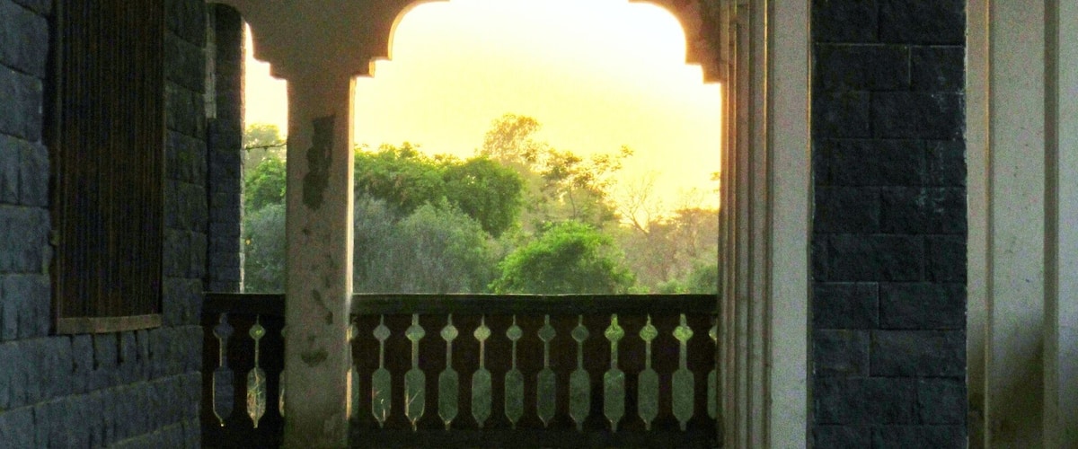 An arched corridor with a wooden floor, brick walls, and a railing overlooking greenery.