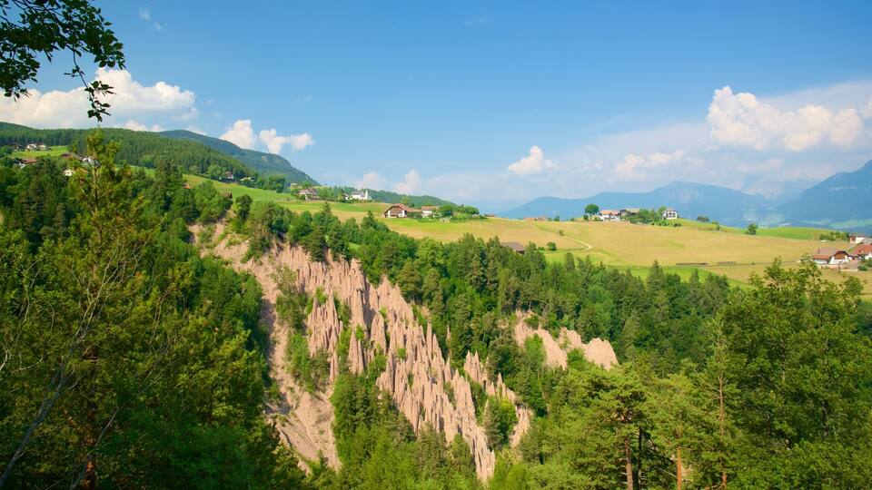 A mountainous landscape with scattered houses, dense forests, and a prominent rocky cliff.