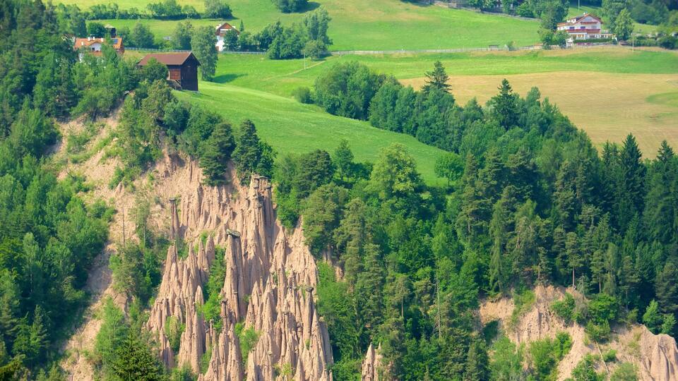 A mountainous landscape with a forested area, a rocky cliff, and a few buildings.
