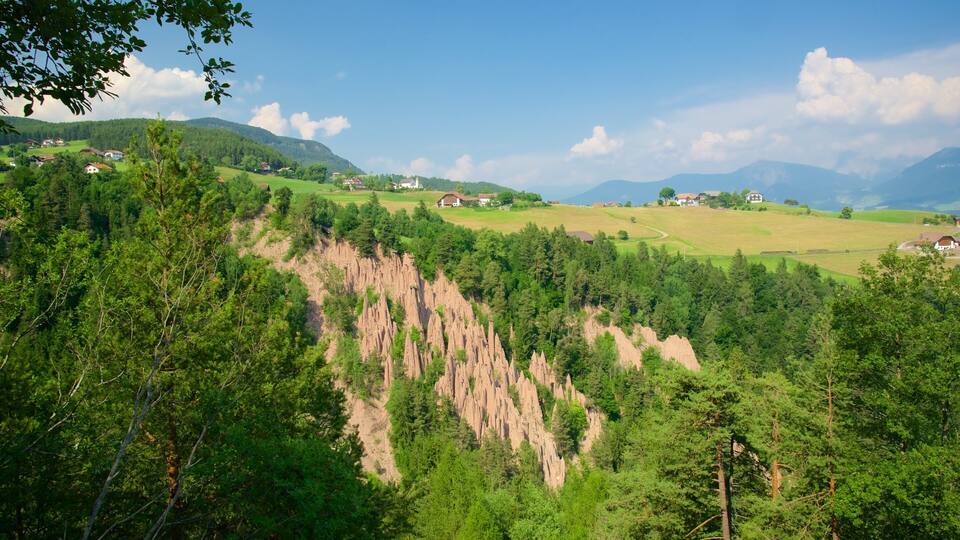 A mountainous landscape with green fields, scattered houses, and a prominent rocky cliff.