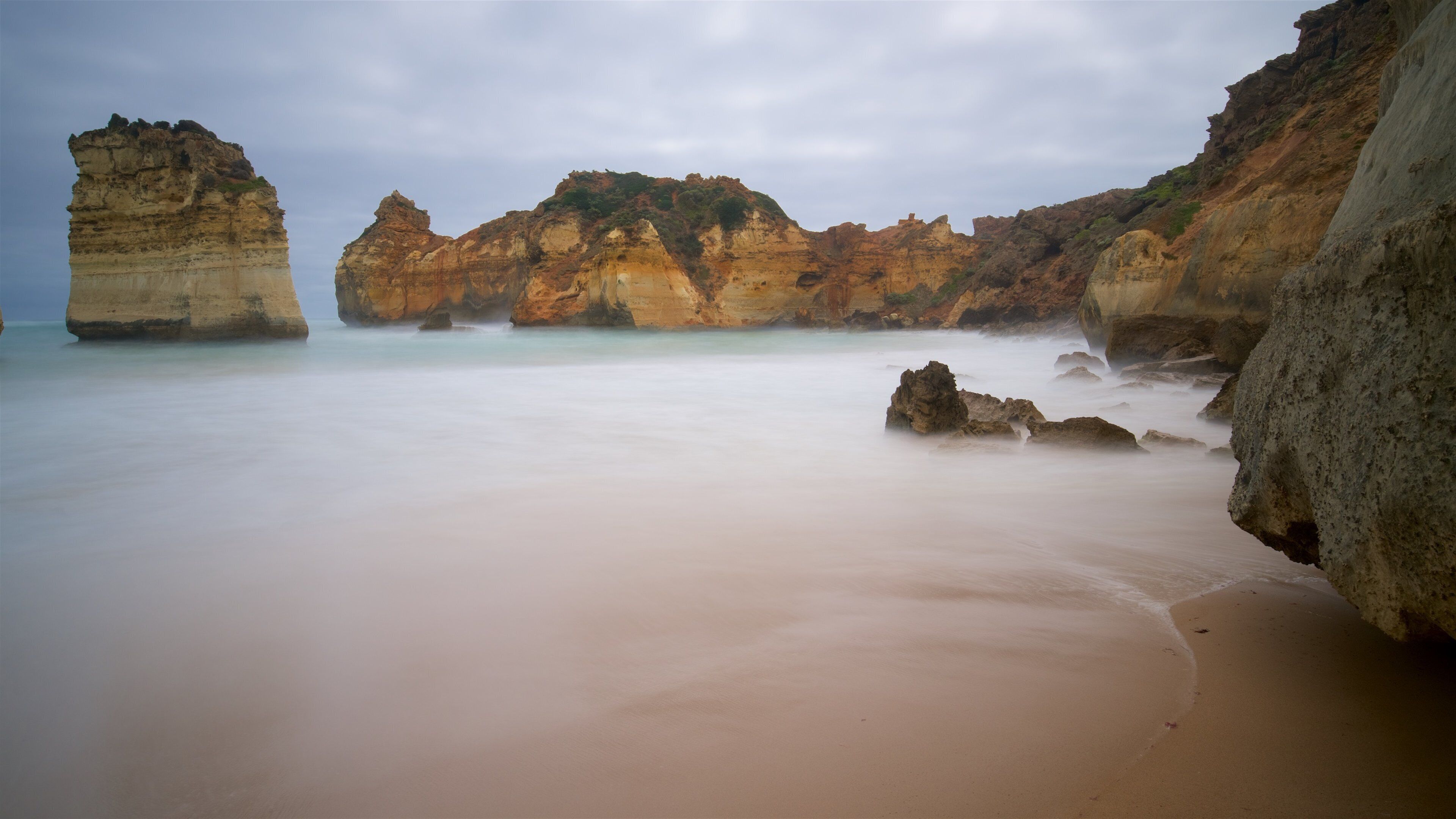 A coastal landscape with layered rock formations and a sandy beach.