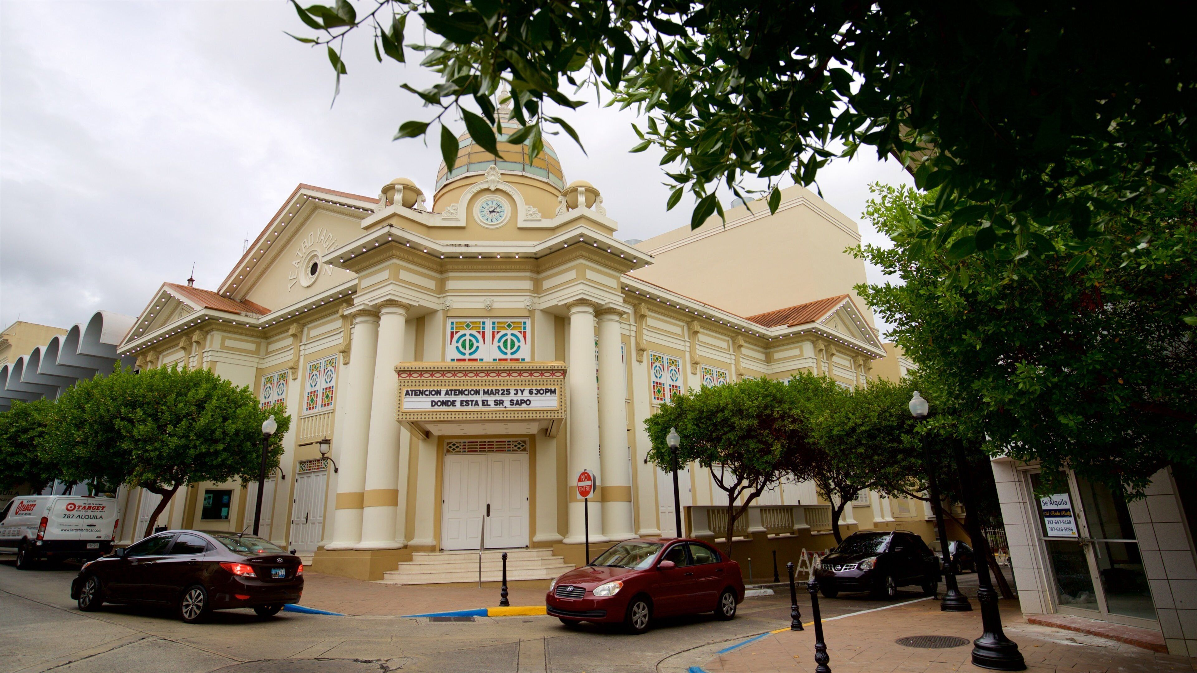 A church with a dome and columns, surrounded by trees and parked cars.