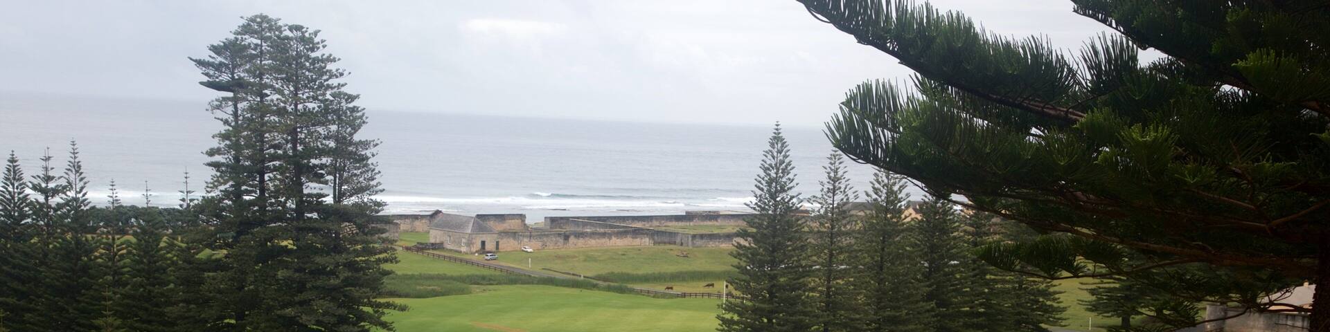 A coastal fort with a large building surrounded by a stone wall, overlooking the ocean.