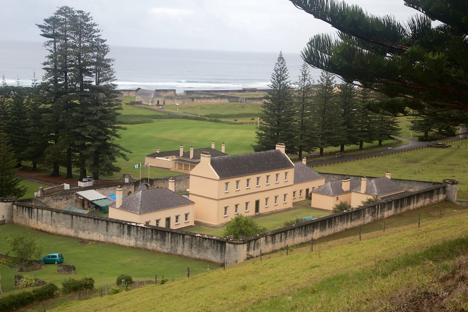 A coastal fort with a large building surrounded by a stone wall, overlooking the ocean.