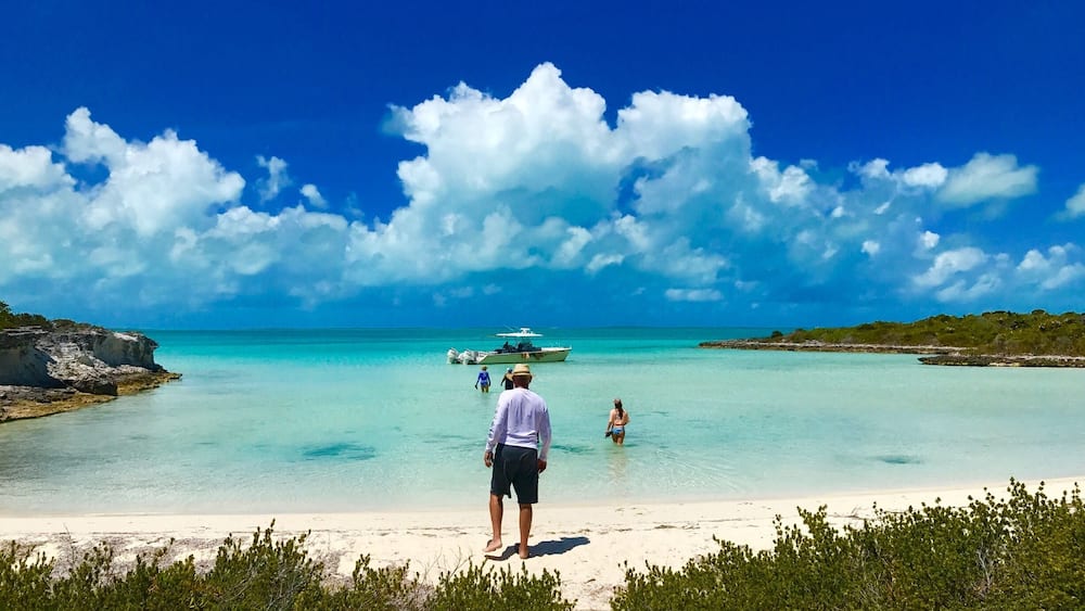 Ein Strand mit klarem türkisblauem Wasser, einem Sandufer und einem Boot in der Ferne.