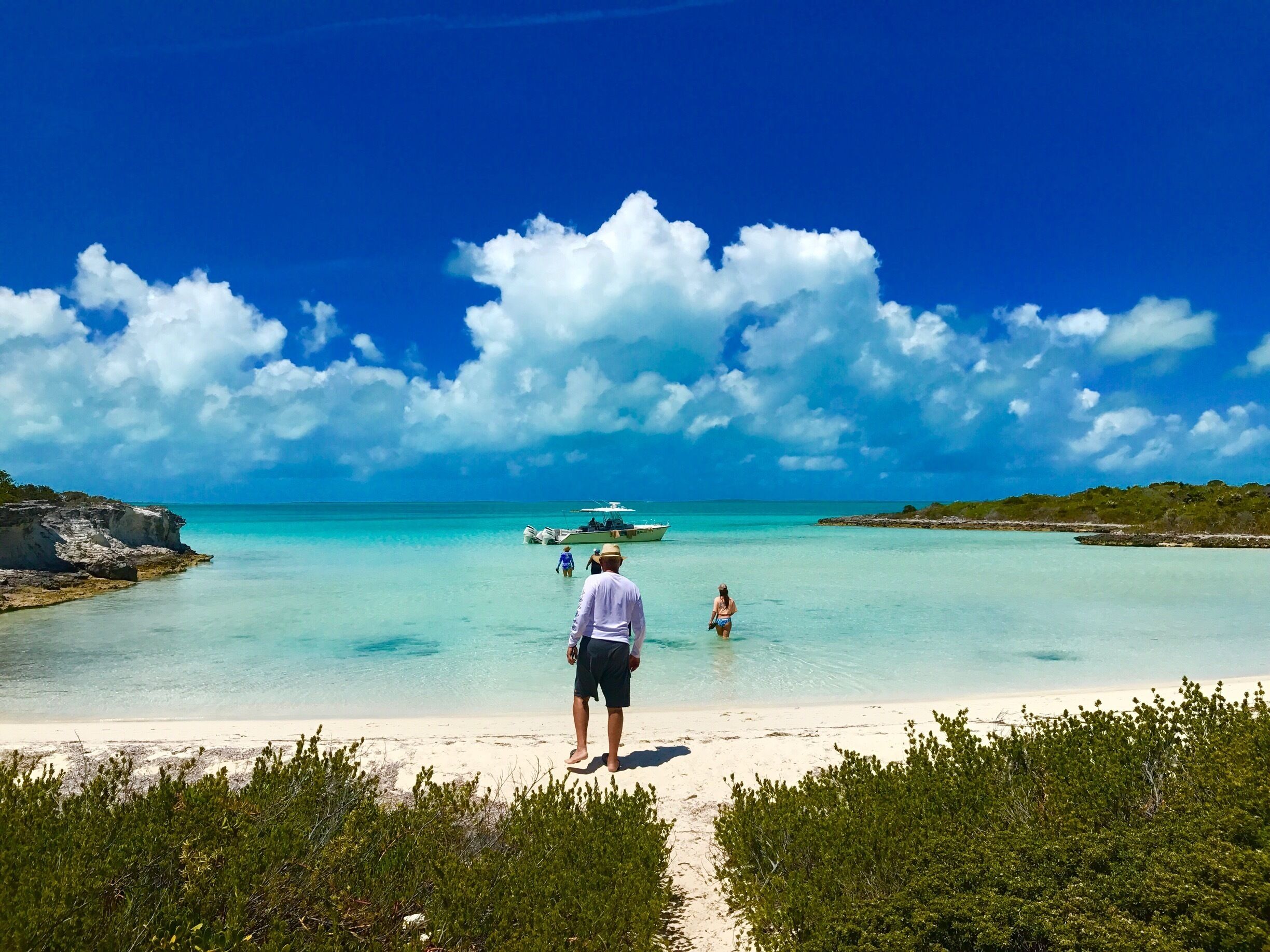 A beach with clear turquoise water, a sandy shore, and a boat in the distance.