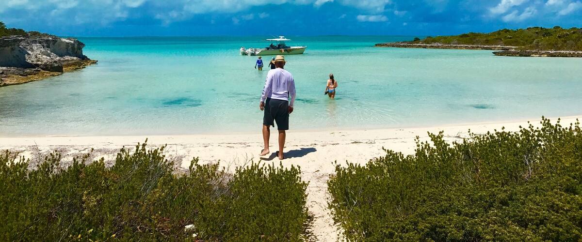 A beach with clear turquoise water, a sandy shore, and a boat in the distance.