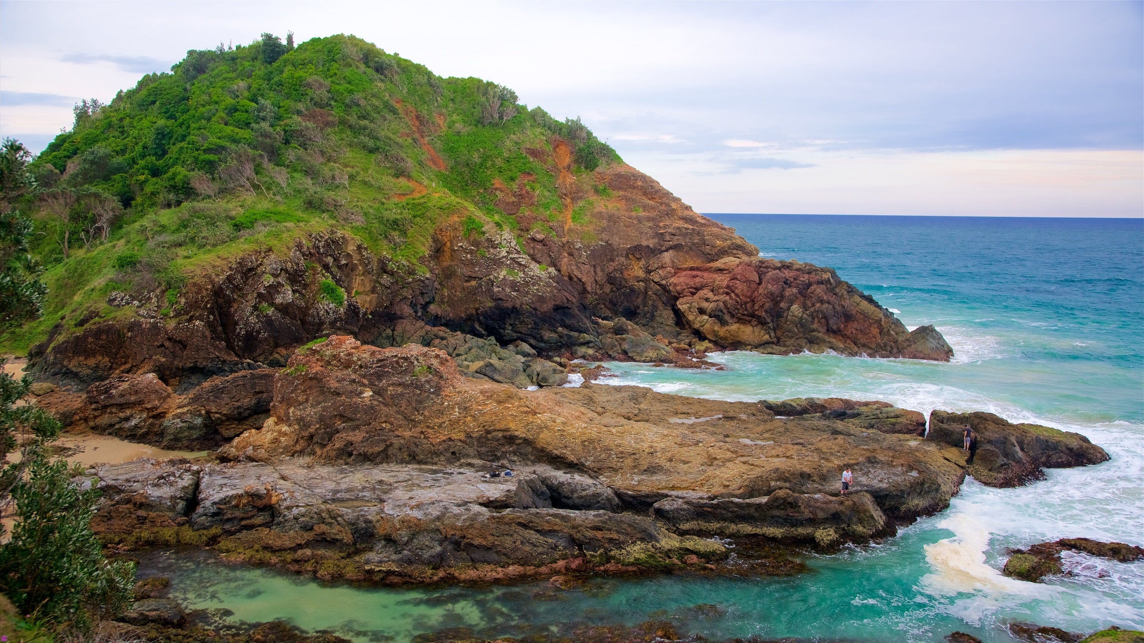 A rocky coastline with a lush green hill and turquoise waters.