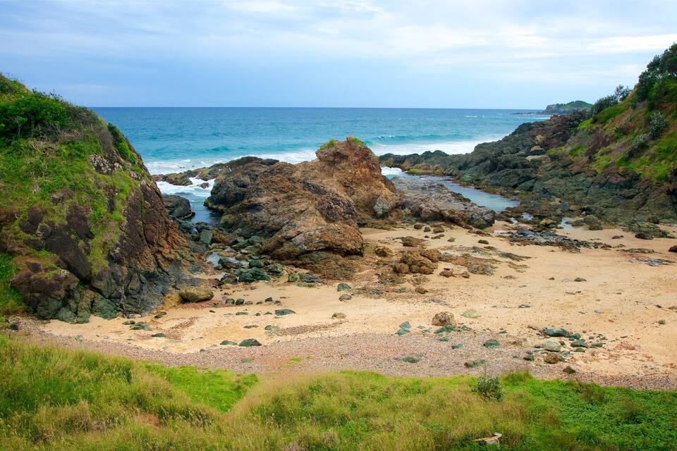 A rocky coastline with a sandy beach and green hills.