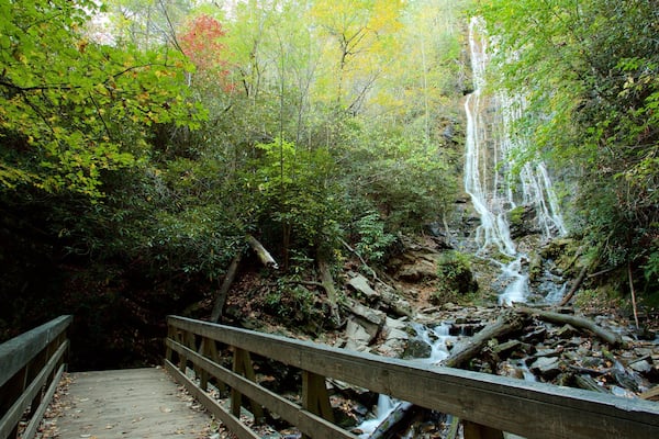 A wooden bridge over a rocky stream with a waterfall in a forested area.