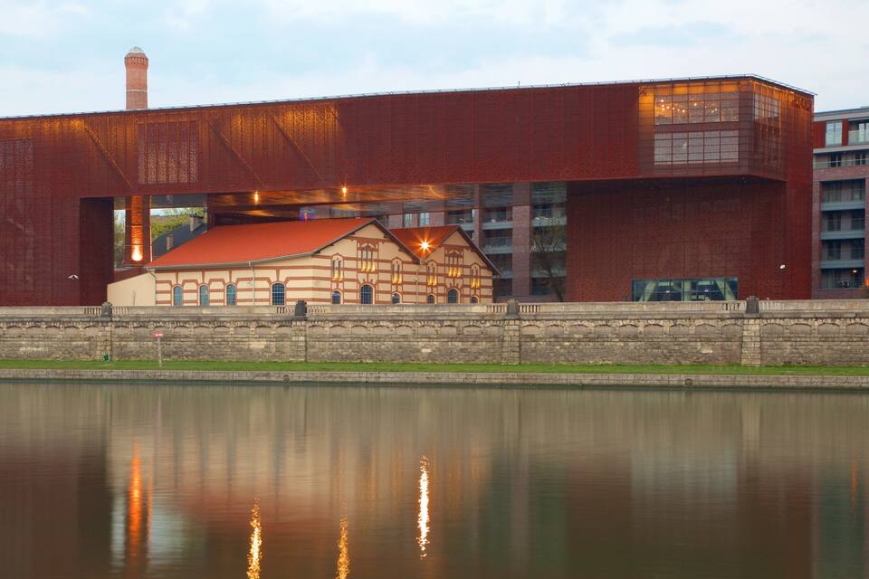 A large industrial building with a red facade and a smaller traditional building with a red roof in front of it.
