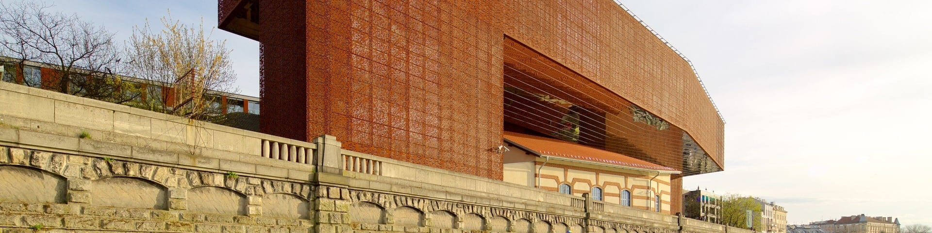 A large red brick building with a modern design, a stone wall in front, and a pathway leading to it.