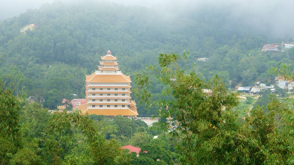 A traditional multi-tiered pagoda surrounded by lush greenery and a misty mountain backdrop.