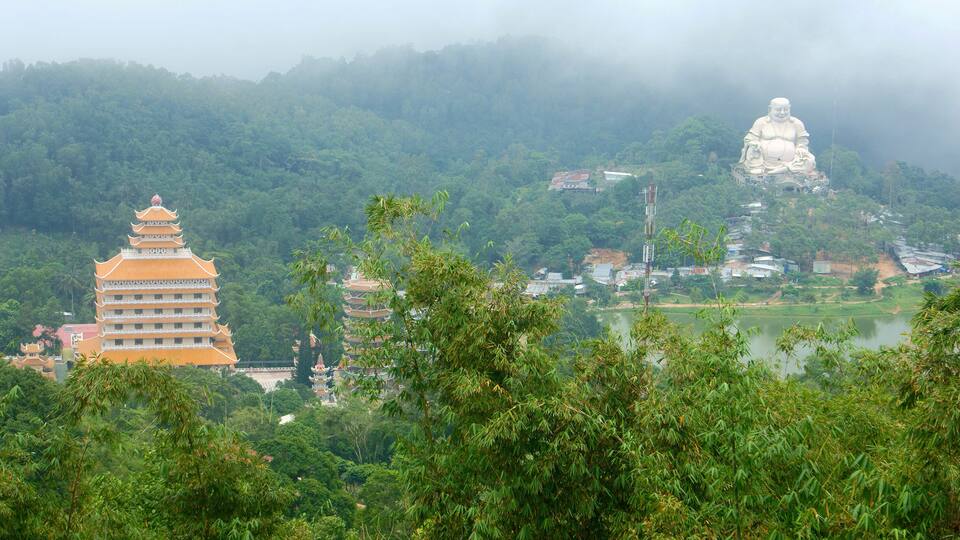 A pagoda and a large Buddha statue in a lush, mountainous landscape.