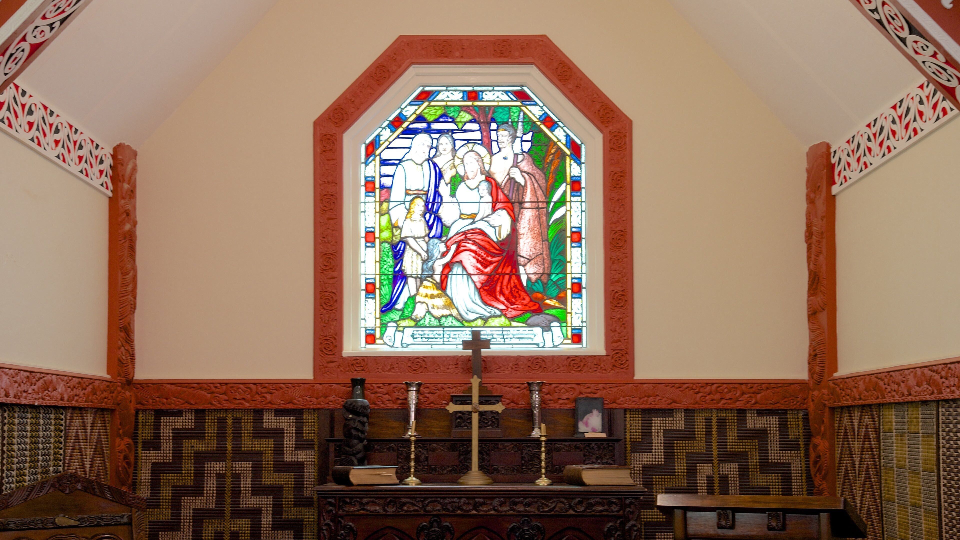 A stained glass window with religious figures, a wooden altar, and patterned wall panels.
