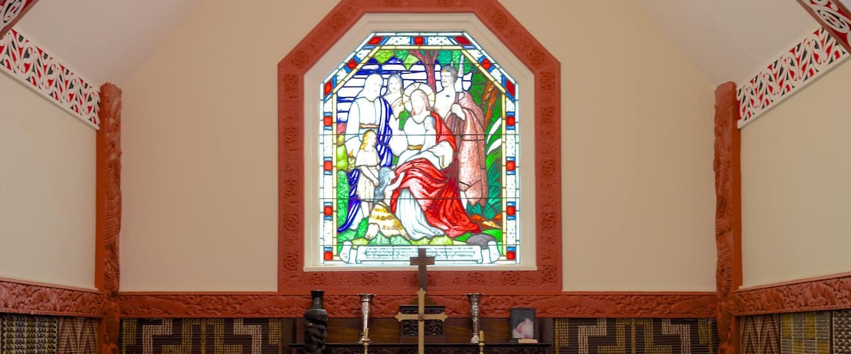 A stained glass window with religious figures, a wooden altar, and patterned wall panels.