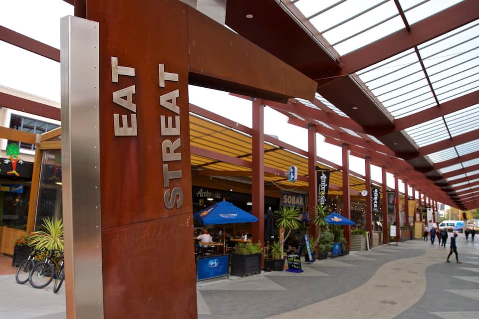 Una zona peatonal techada con un llamativo letrero que dice 'EAT STREAT', mesas al aire libre y diversas tiendas.