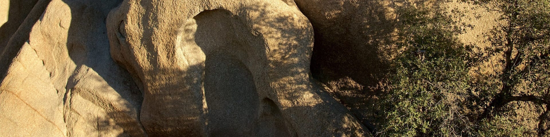 A large rock formation with a prominent hole and surrounding vegetation.