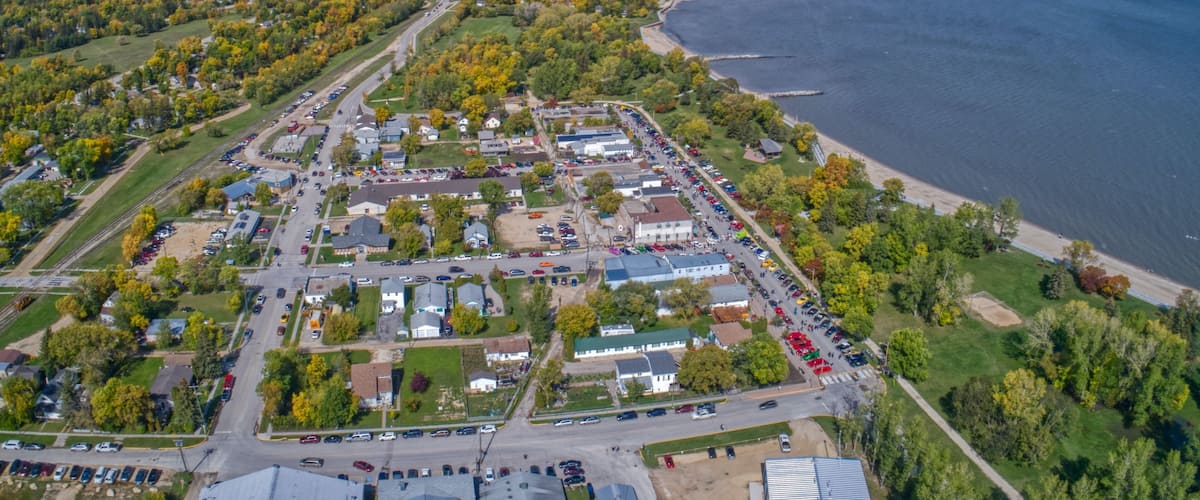 An aerial view of a coastal town with a marina, dense forest, and a clear sky.