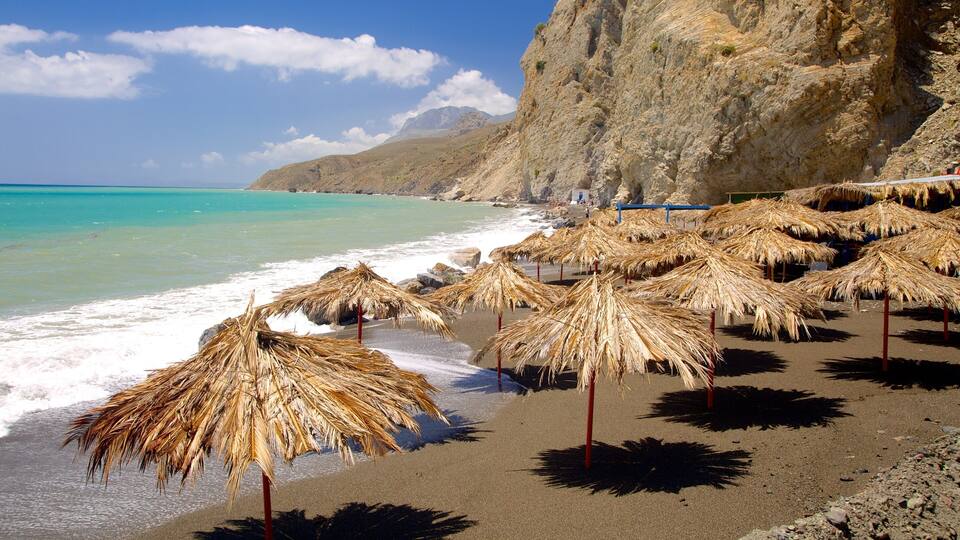 A beach with thatched umbrellas and rocky cliffs.