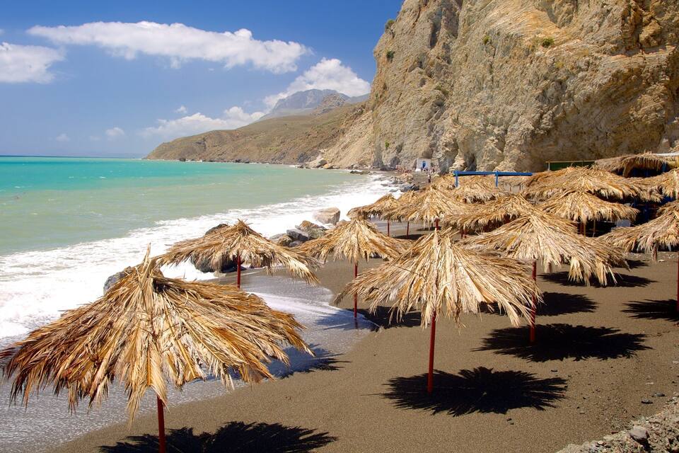 A beach with thatched umbrellas and rocky cliffs.