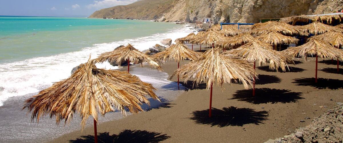 A beach with thatched umbrellas and rocky cliffs.