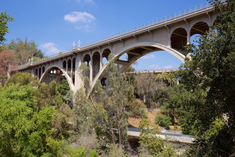 A large stone bridge with multiple arches, surrounded by dense greenery and trees.