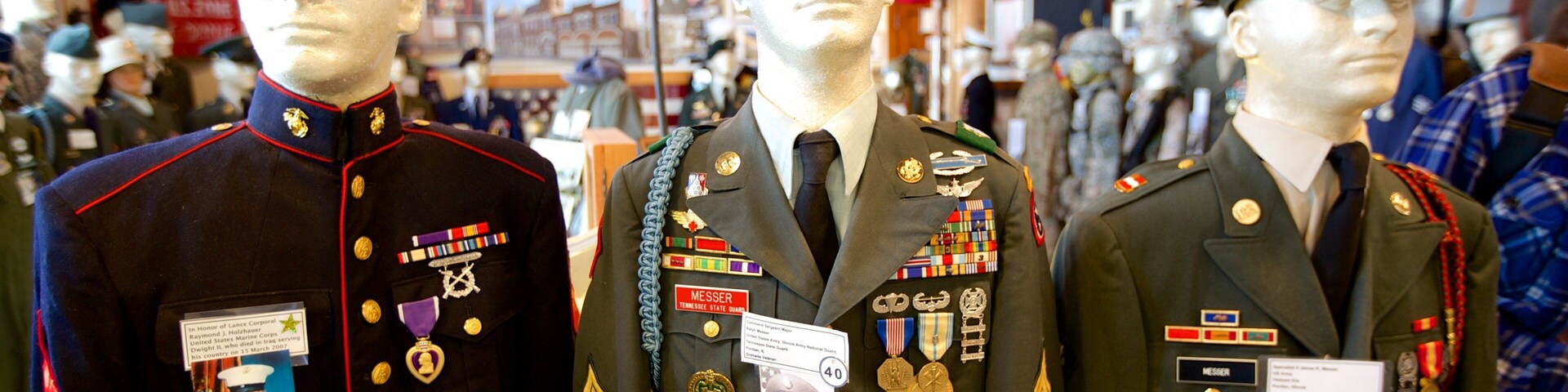 Mannequins vestidos com uniformes militares, medalhas e etiquetas com nomes.
