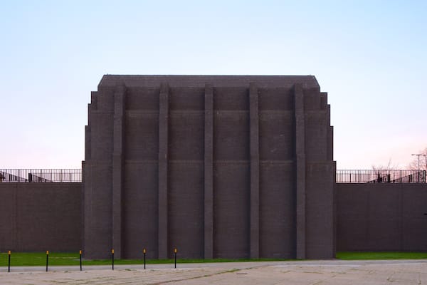 Um edifício grande e retangular de tijolos, com telhado plano e janelas verticais.