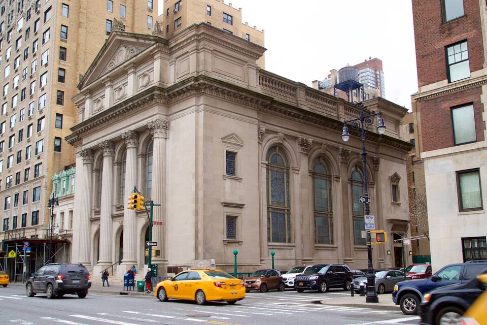 Una intersección concurrida con un edificio histórico que presenta columnas ornamentadas y ventanas amplias.