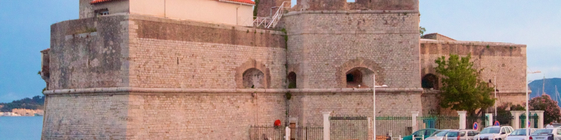A historic stone fortress with a red-tiled roof, situated by a calm body of water.