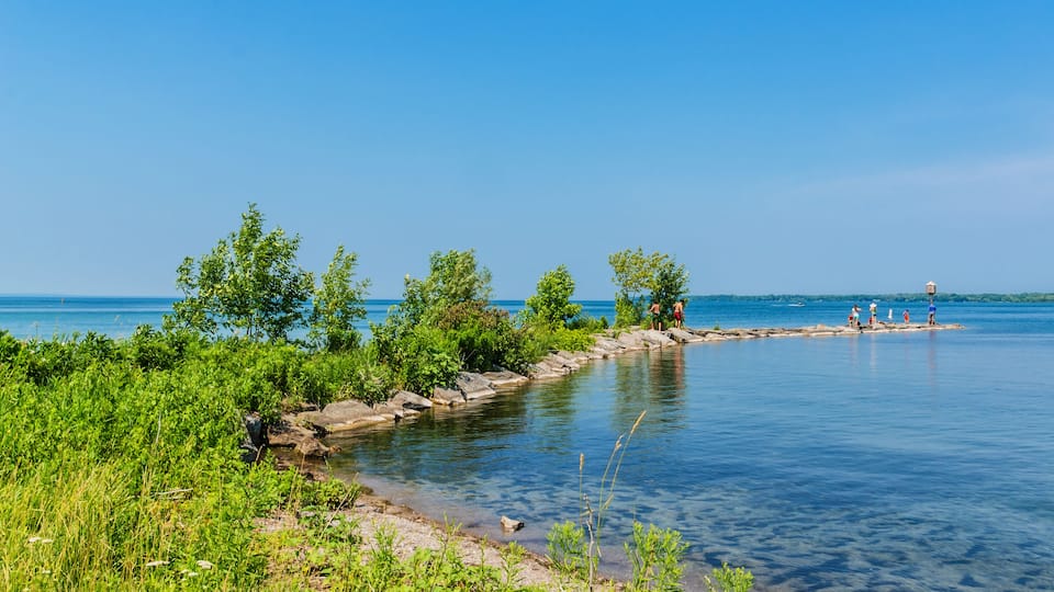 A calm lake with clear blue water, surrounded by lush greenery and rocky shores.