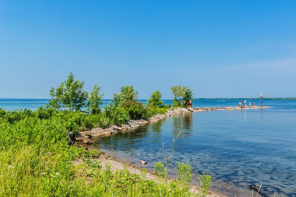 A calm lake with clear blue water, surrounded by lush greenery and rocky shores.