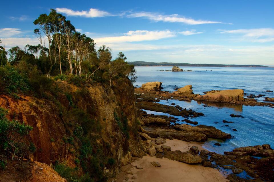 Un paisaje costero con afloramientos rocosos, playa arenosa y vegetación densa.