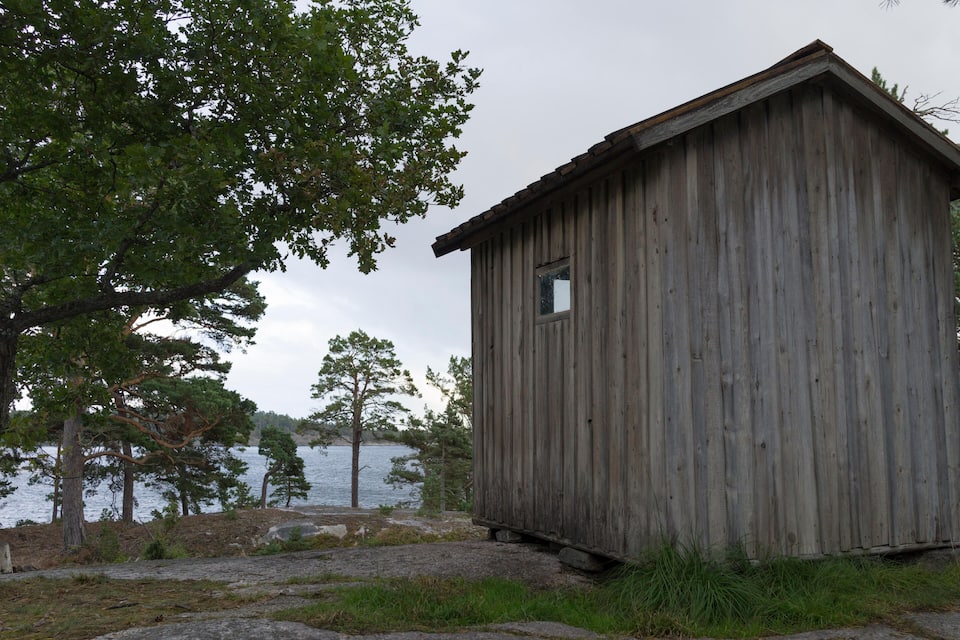 A wooden cabin by a lake with trees and rocks around.