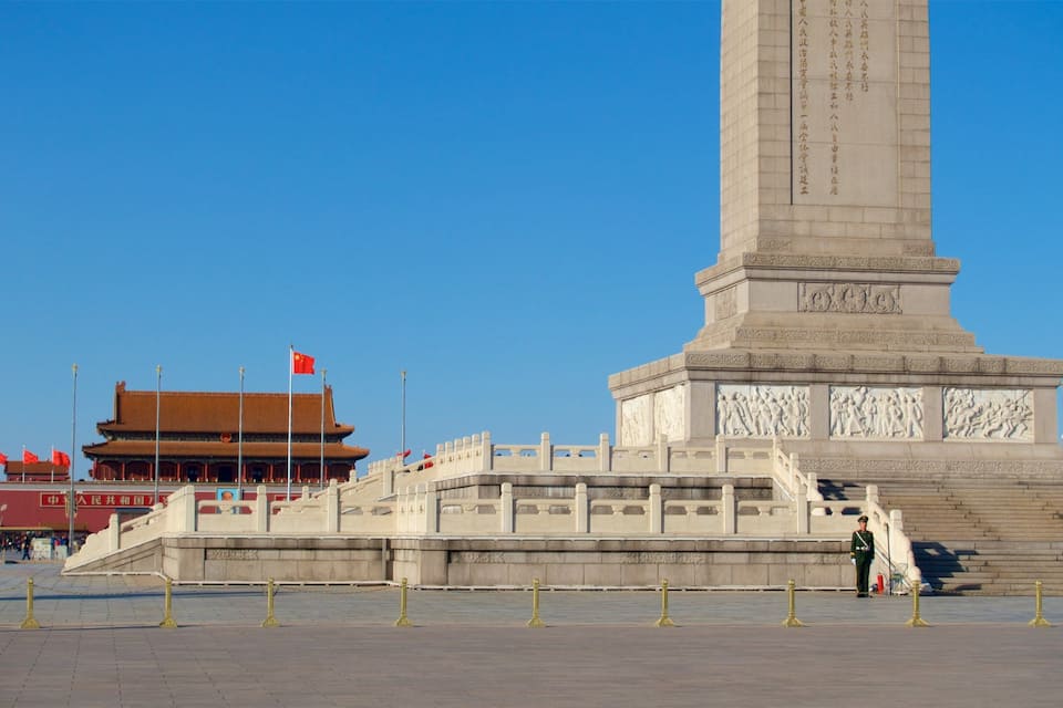 Um grande monumento com inscrições, um edifício tradicional com telhado vermelho e um céu azul límpido.