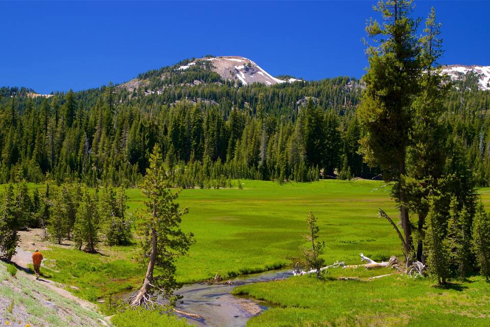 A mountainous landscape with a green valley, a stream, and a person hiking.
