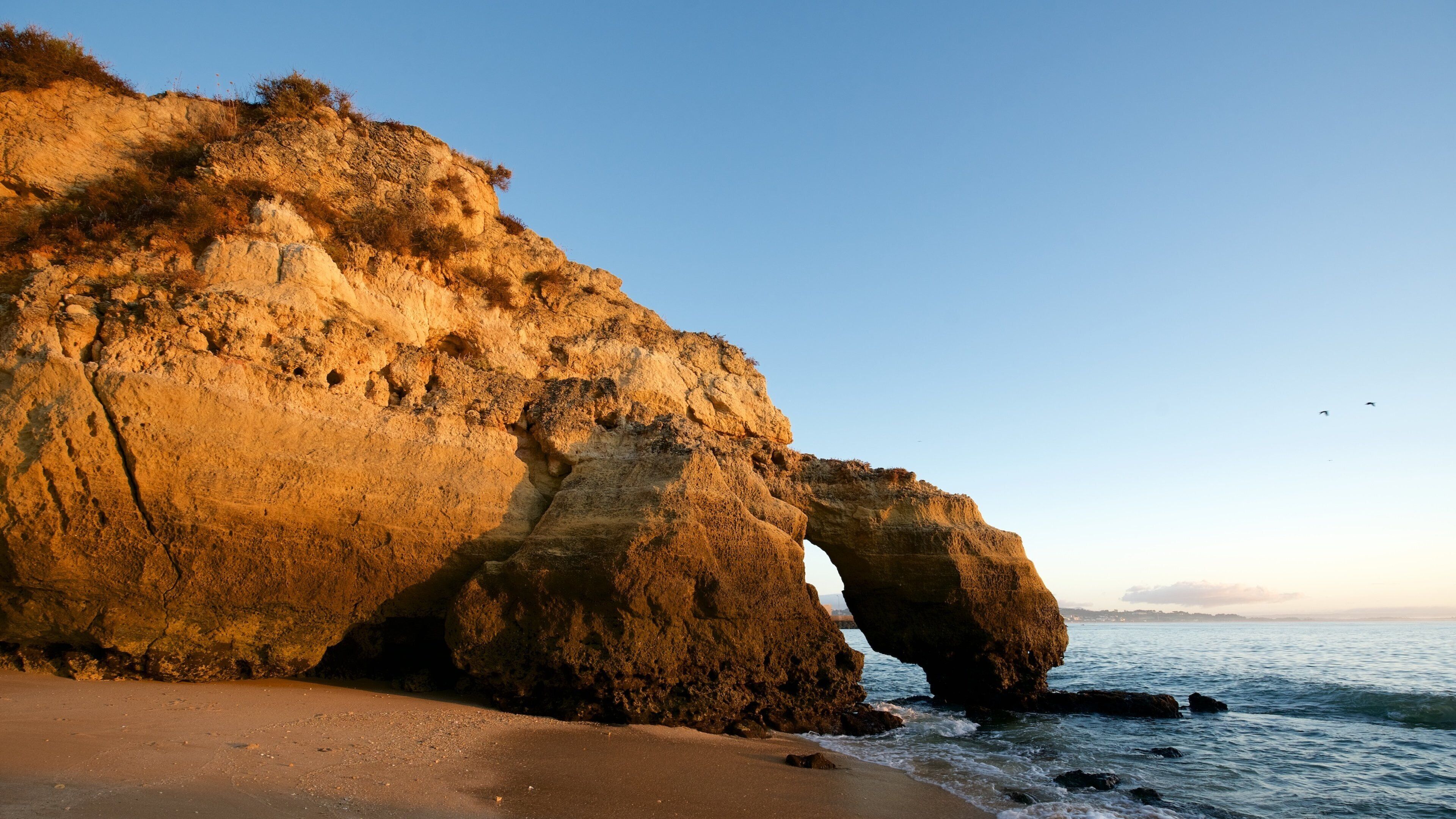 Formação rochosa costeira com um arco natural e uma praia de areia.