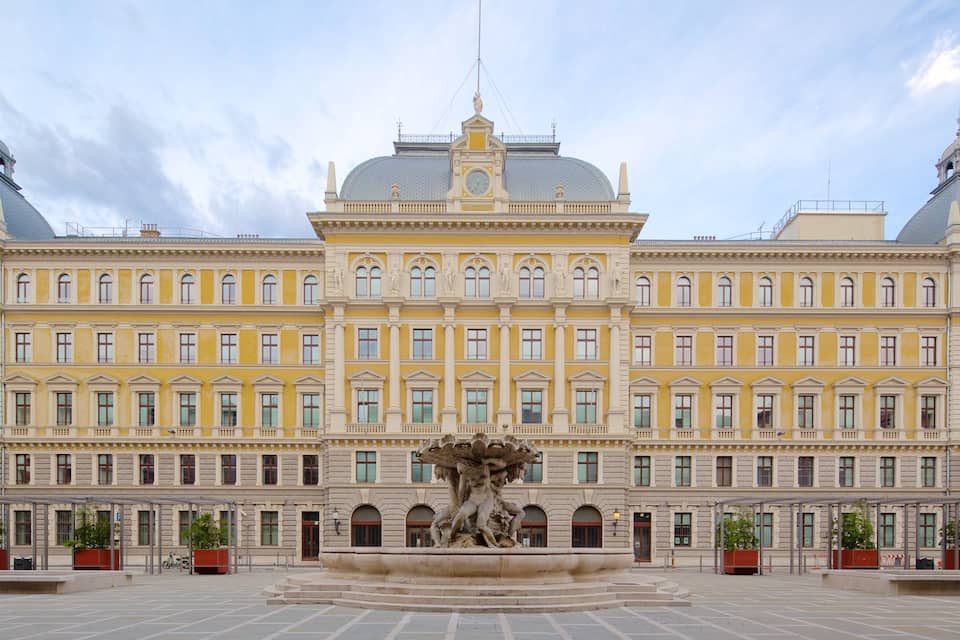 Ein großes gelbes Gebäude mit einer zentralen Fontäne und zwei Kuppeln.