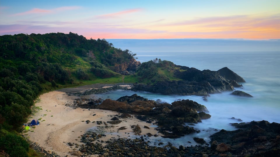 A coastal landscape with a sandy beach, rocky outcrops, and a lush green hillside.