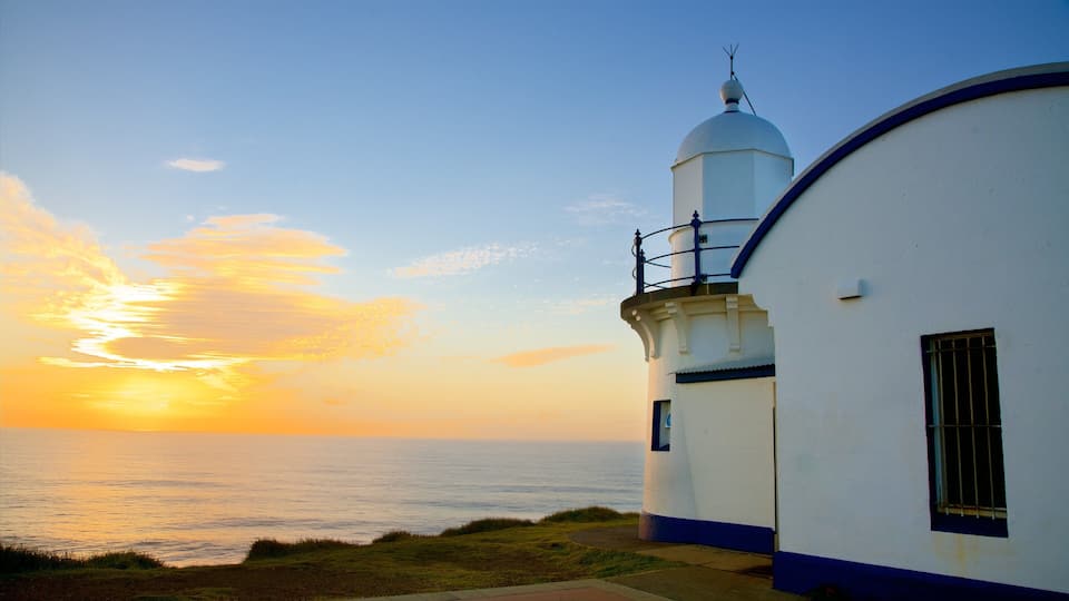 A lighthouse with a white dome and blue trim, overlooking the ocean at sunset.