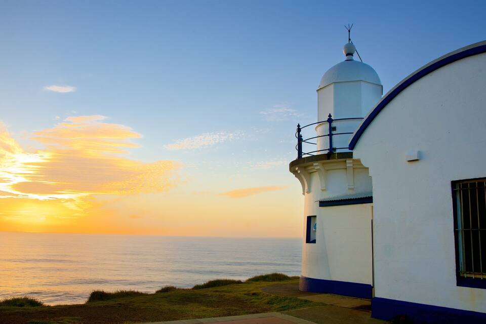 A lighthouse with a white dome and blue trim, overlooking the ocean at sunset.