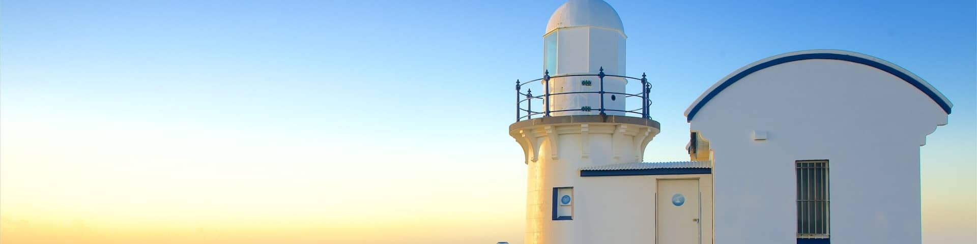A lighthouse with a white and blue structure, a grassy hill, and the ocean in the background.
