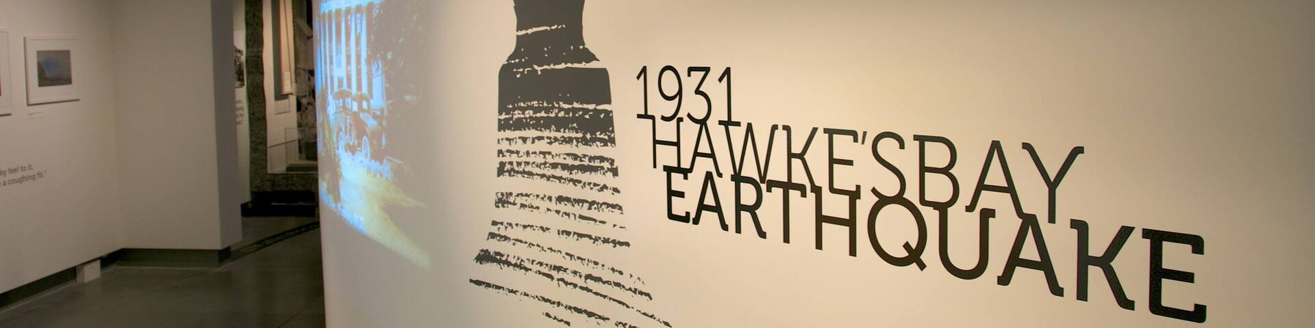 Pared con el texto '1931 HAWKESBAY EARTHQUAKE' y una proyección de un edificio.