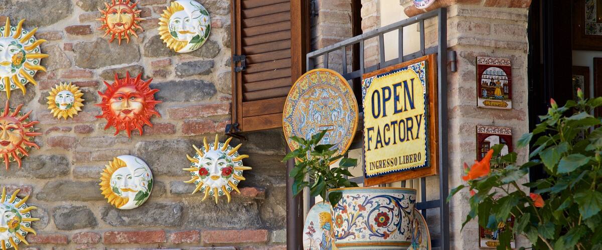 Fachada rústica decorada con coloridos máscaras de sol de cerámica, un letrero que dice “OPEN FACTORY” y cerámica tradicional.