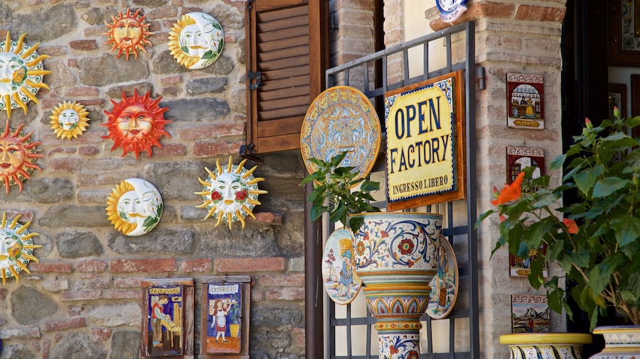 A rustic building facade adorned with colorful ceramic sun masks, a sign reading "OPEN FACTORY," and traditional pottery.