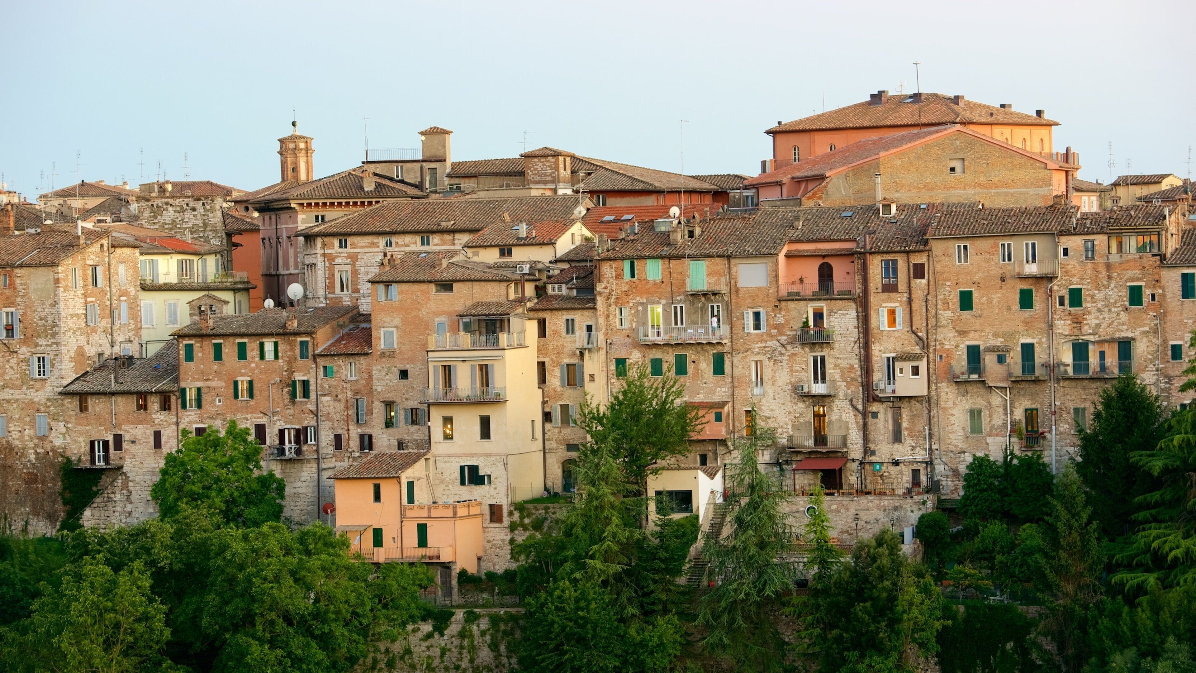 Un pueblo histórico con edificios de varios pisos, algunos con balcones y contraventanas verdes, rodeado de abundante vegetación.